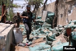 FILE - Rebel fighters of Jaysh al-Islam (Army of Islam) carry their weapons as they walk along a military post used by forces loyal to Syria's President Bashar al-Assad in Deir Salman frontline, near the highway of Damascus international airport.