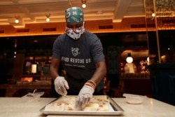 Sharon Holm, a volunteer from Food Rescue US, prepares cold cuts for sandwiches at Marcus Samuelsson's Red Rooster Restaurant during the new coronavirus pandemic, Monday, April 6, 2020, in the Overtown neighborhood of Miami. (AP Photo/Lynne Sladky)