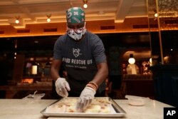 Sharon Holm, a volunteer from Food Rescue US, prepares cold cuts for sandwiches at Marcus Samuelsson's Red Rooster Restaurant during the new coronavirus pandemic, Monday, April 6, 2020, in the Overtown neighborhood of Miami. (AP Photo/Lynne Sladky)