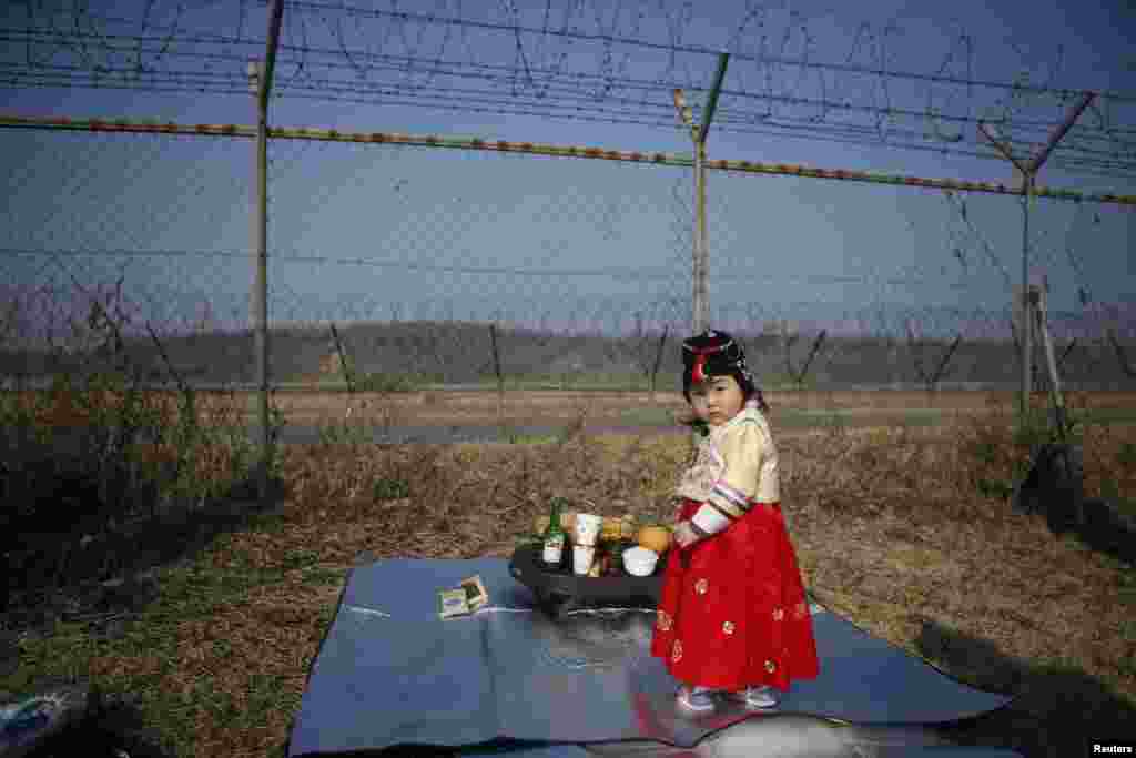Một bé gái mặc áo Hanbok, trang phục truyền thống của Hàn Quốc, đứng trước một hàng rào kẽm gai, trong lúc cha mẹ chuẩn bị làm lễ tưởng niệm cho những thân nhân người Bắc Triều Tiên, gần khu phi quân sự ngăn cách hai miền Triều Tiên, ở Paju, nhân dịp Seolnal, ngày Tết âm lịch của Hàn Quốc.