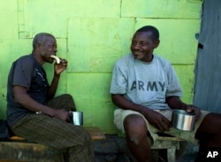 FILE - "Bayakou," or human waste cleaner, Auguste Augustin, left, visits with a friend in Port-au-Prince's La Saline slum, Haiti, Dec. 25, 2016.