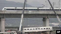 A high speed bullet train runs past a railway bridge as workers use cranes to lift a wrecked carriage onto a truck after two trains crashed and derailed in Wenzhou, Zhejiang province, July 26, 2011.