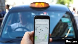 A photo illustration shows a person holding a phone with an Uber app and a black cab in London, Britain, June 26, 2018.