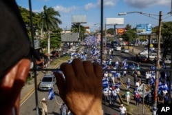 FILE - An individual watches from above as protestors march below during an anti-government protest in Managua, Nicaragua, Aug. 11, 2018.