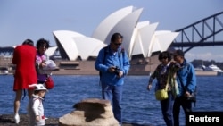 Chinese tourists stand on rocks on the edge of Sydney Harbour as they take pictures of themselves in front of the Sydney Opera House in Sydney, Australia.