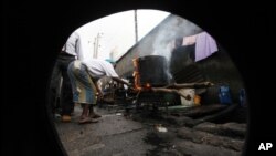 FILE - July 11, 2011 photo, A woman is seen through a broken-down car tire, as she uses firewood to prepare a meal in Lagos, Nigeria.(AP Photo/Sunday Alamba)