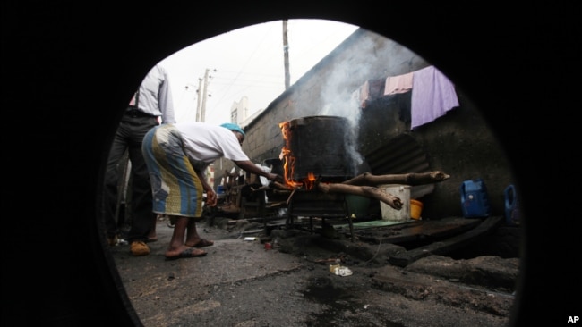 FILE - July 11, 2011 photo, A woman is seen through a broken-down car tire, as she uses firewood to prepare a meal in Lagos, Nigeria.(AP Photo/Sunday Alamba)
