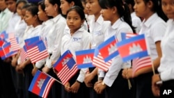 FILE - Students from a local high school carry the U.S. national flag and Cambodia's national flag as they await the arrival of U.S. first lady Michelle Obama and Bun Rany, the first lady of Cambodia, Saturday, March 21, 2015, on the outskirts of Siem Reap, Cambodia. 