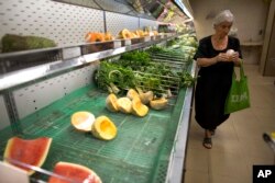 A woman looks at the price of a melon at a supermarket in Caracas, Venezuela, Friday, March 23, 2018.