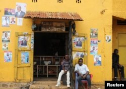 Men sit in front of election posters in Beni, North Kivu Province of Democratic Republic of Congo, Dec. 5, 2018.