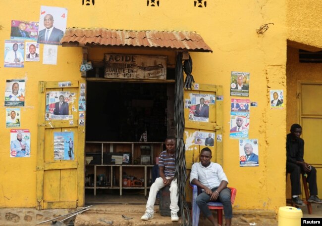 Men sit in front of election posters in Beni, North Kivu Province of Democratic Republic of Congo, Dec. 5, 2018.