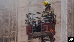 Two women are rescued by a firefighter in a bucket crane outside the World Trade Centre located in the city's popular Causeway Bay shopping district of Hong Kong, Dec. 15, 2021.