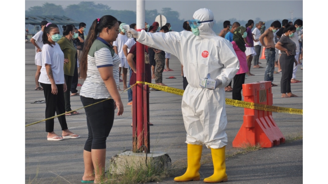 Seorang petugas kesehatan memeriksa suhu pekerja migran Indonesia yang tiba dari Malaysia selama karantina untuk mencegah penyebaran Covid-19, di pangkalan udara Soewondo di Medan, Sumatra Utara, 11 April 2020.