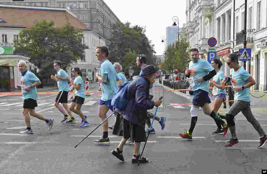 An elderly woman walks past participants of a street run in Warsaw, Poland.