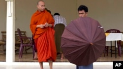 A Buddhist devotee holds an umbrella for controversial Buddhist monk Wirathu (L), who is accused of instigating sectarian violence between Buddhists and Muslims through his sermons, , near Rangoon, Burma, June 14, 2013.