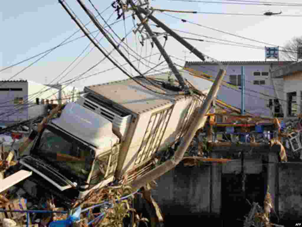 A huge trailer stuck in an narrow canal leans over debris at a port in Sendai, northern Japan, one day after a massive Tsunami triggered by a huge earthquake hit northern Japan Saturday, March 12, 2011.