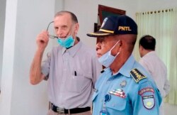 Seorang petugas polisi mengawal Richard Daschbach, tengah, seorang mantan misionaris dari Pennsylvania, A.S. pada saat kedatangannya untuk diadili di gedung pengadilan di Oecusse, Timor Leste. (Foto: AP)