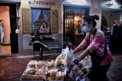 A snacks vendor wearing a mask and face shield to try to halt the spread of the Covid-19 coronavirus walks past an Elvis statue in a face mask at a market in Bangkok on January 19, 2021. (Photo by Lillian SUWANRUMPHA/AFP)