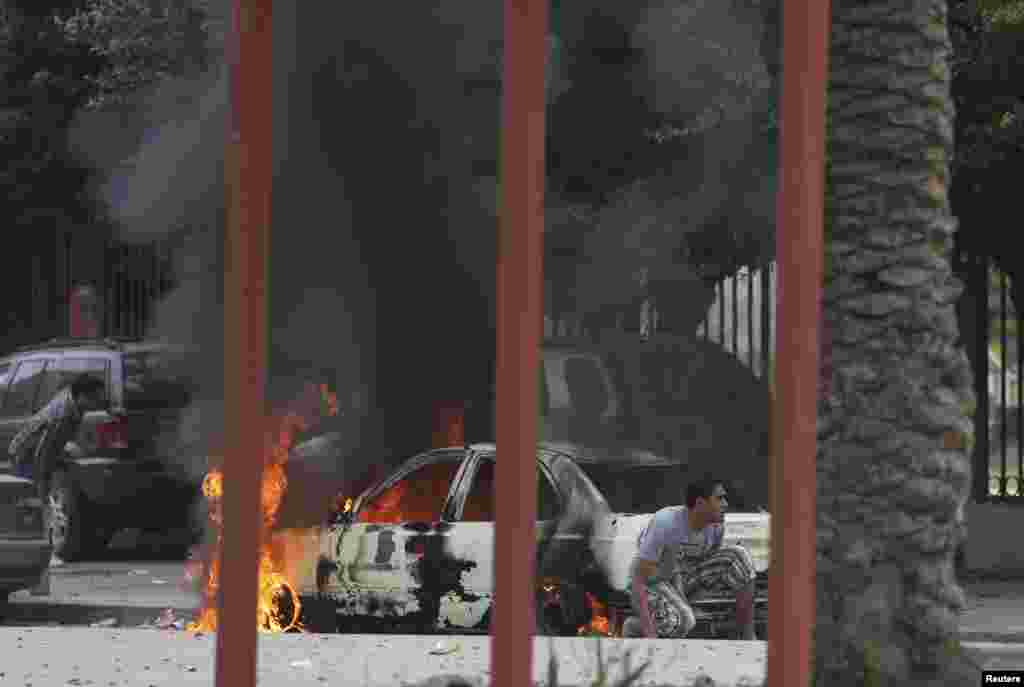 Residents hide near a burning car during clashes between members of Islamist militant group Ansar al-Sharia and a Libyan army special forces unit in the Ras Obeida area in Benghazi.