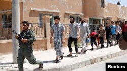 FILE - Islamic State prisoners walk behind a Kurdish policeman in Ain Issa village, north of Raqqa, Syria, June 24, 2017.