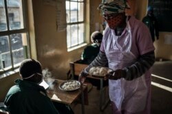 Siswa kelas 7 SMP Sitoromo di Sterkspruit, duduk di kelas mereka saat seorang juru masak membagikan hidangan susu dan bubur jagung, 6 Juli 2020.