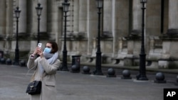 Un turista cubierta con una máscara de sanidad se hace una selfie frente al museo del Louvre el viernes 28 de febrero de 2020 en París. El museo cerró sus puertas el domingo 1 de marzo, por temores al coronavirus.