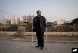 FILE - Zhou Wangyan, head of the Liling city land resources bureau, stands with crutches near a plot of land under development in Liling city in central China's Hunan province.