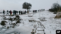 FILE - Migrants cross a frozen stream as they walk through a snowstorm from the Macedonian border into Serbia, near the village of Miratovac, Serbia, Jan. 18, 2016.
