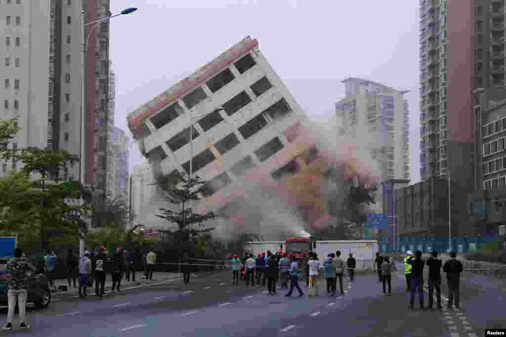 People watch the controlled demolition of an eight-storey &quot;nail house&quot; that stood on a road in Haikou, Hainan province, China.
