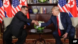 Le président des États-Unis, Donald Trump, serre la main du dirigeant nord-coréen Kim Jong Un lors de leurs premières rencontres au resort de Capella sur l'île de Sentosa, le 12 juin 2018 à Singapour.