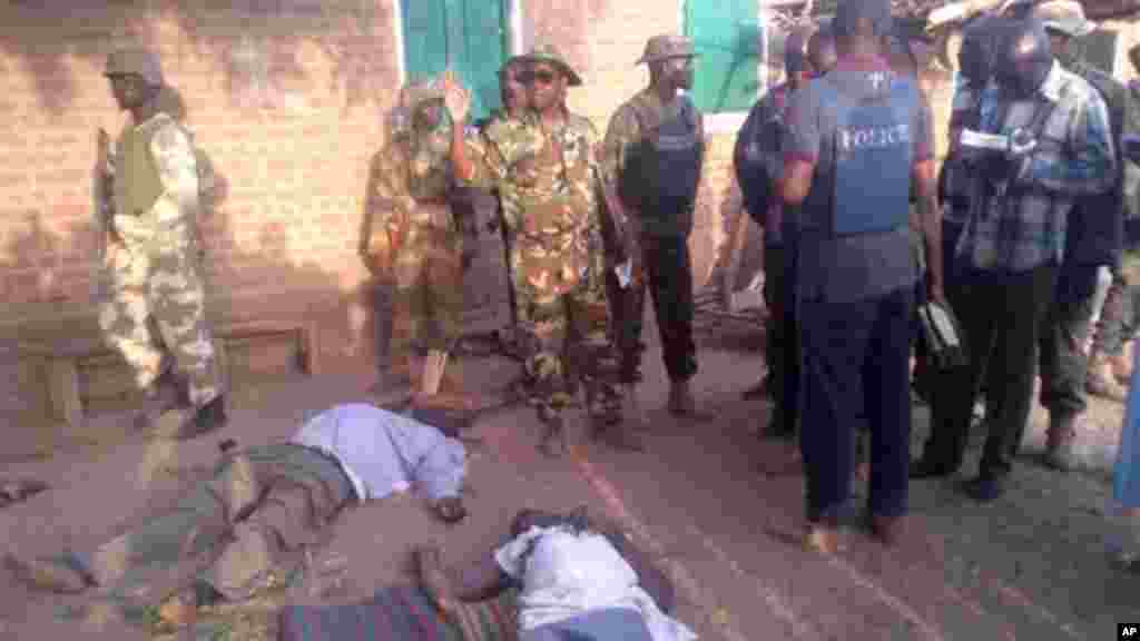 In this photo taken with a mobile phone, Tuesday, May. 7, 2013, soldiers and journalist looks at bodies of prison officials killed by Islamic extremist during heavy fighting in Bama, Nigeria.