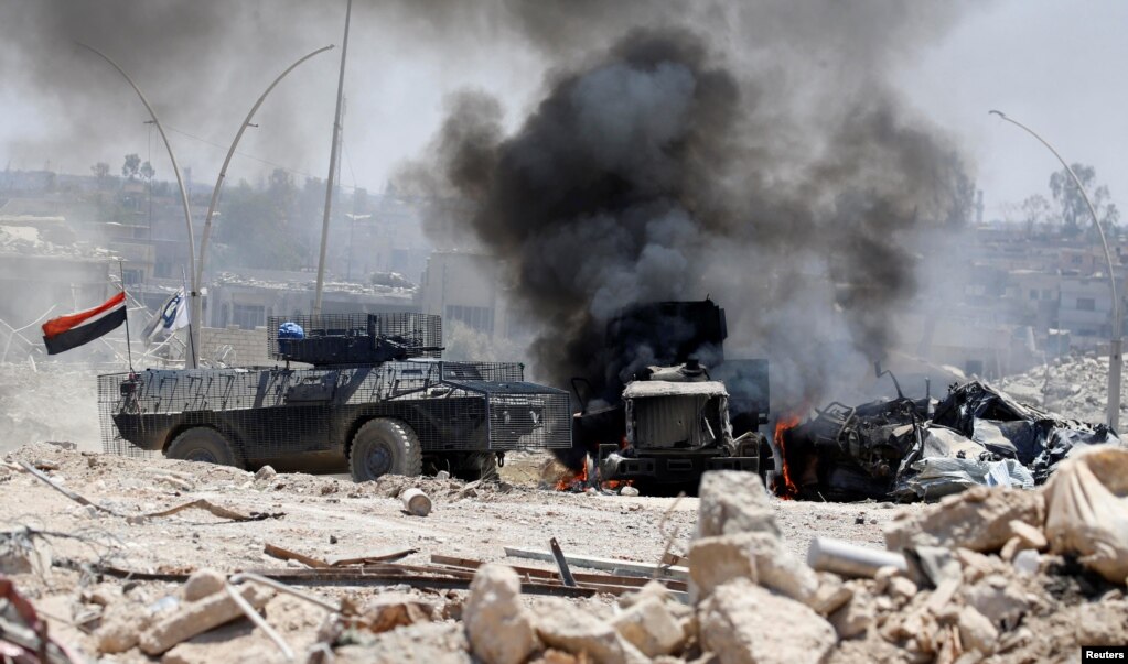 이라크군 장갑 전투차량이 모술 서부지역에서 이슬람 수니파 무장단체 ISIL의 공격으로 불타고 있는 트럭 옆을 지나고 있다.