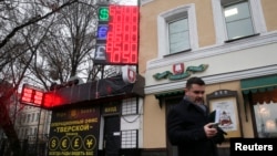 一名路人12月16日行經莫斯科一建築前﹐背後電子報表顯示盧布再創新低。