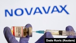A woman holds a small bottle labeled with a "Coronavirus COVID-19 Vaccine" sticker and a medical syringe in front of displayed Novavax logo in this illustration taken, October 30, 2020. REUTERS/Dado Ruvic/File Photo
