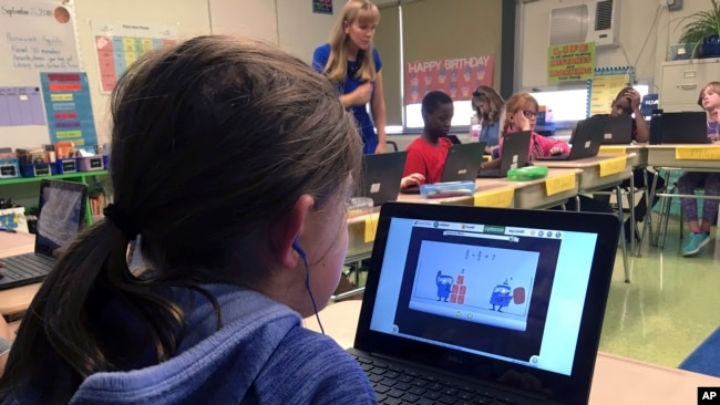 In this Sept. 20, 2018 photo, fifth grade student Ashlynn De Filippis, left, works math problems on the DreamBox system as teacher Heather Dalton, center rear, works with other students in class at Charles Barnum Elementary School in Groton, Conn. (AP Photo)