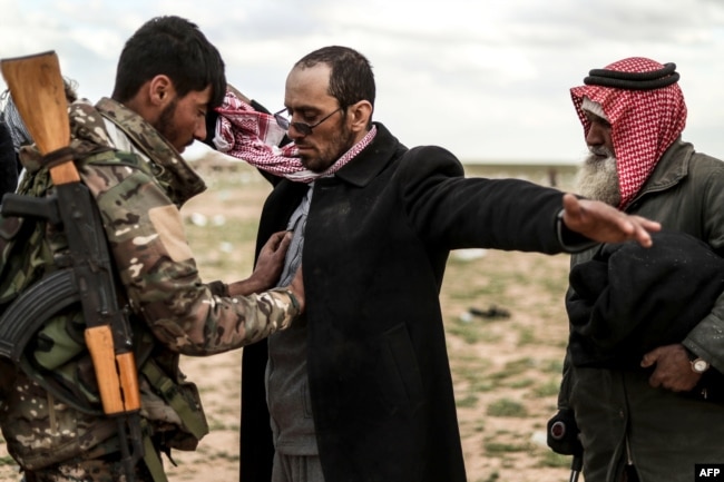 Men suspected of being Islamic State are searched by a member of the Kurdish-led Syrian Democratic Forces (SDF) after leaving the IS group's last holdout of Baghuz, in Syria's northern Deir Ezzor province, Feb. 27, 2019.