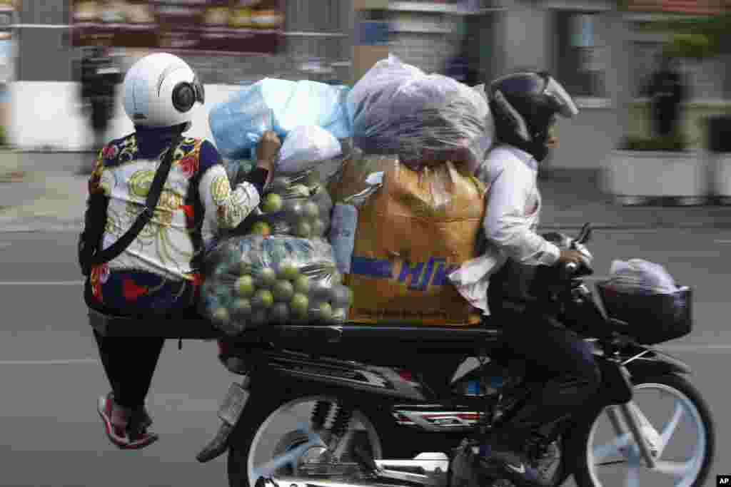 A motorcycle taxi driver carries a vendor on an extended seat on his motorcycle to a market, in Phnom Penh, Cambodia, Aug. 18, 2021.