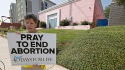 FILE - In this Oct. 2, 2019. file photo, an abortion opponent sings to herself outside the Jackson Women's Health Organization clinic in Jackson, Miss.