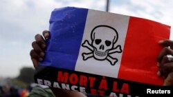 FILE - A supporter holds a flag of France, with the drawing of a skull on it, as he participates in a demonstration called by Mali's transitional government after ECOWAS imposed sanctions, in Bamako, Mali, Jan. 14, 2022. The flag reads "Death to France and allies." 