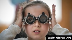 A little girl adjusts testing glasses during an eyesight examination performed by volunteer ophthalmologists working with the humanitarian organization Casa Buna, or Good House, in Nucsoara, Romania, Saturday, May 29, 2021. (AP Photo/Vadim Ghirda)