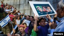 A boy holds a board with the likeness of three teenagers who had been kidnapped in Israel during a memorial service near the United Nations headquarters in New York, June 30, 2014. 