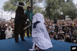 FILE - A Shariah law official whips a woman who is convicted of prostitution during a public caning outside a mosque in Banda Aceh, Indonesia, April 20, 2018.