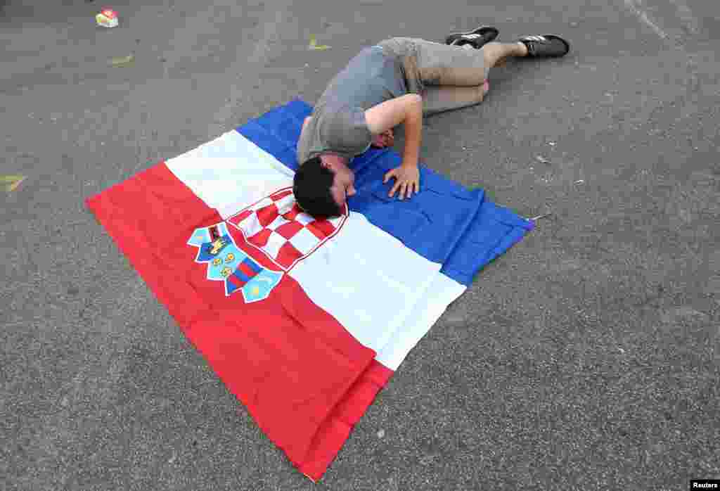 Seorang pendukung timnas Kroasia berbaring di atas bendera Kroasia setelah menyaksikan laga final Piala Dunia 2018 antara Perancis dan Kroasia di alun-alun Kota Zagreb, 15 Juli 2018.