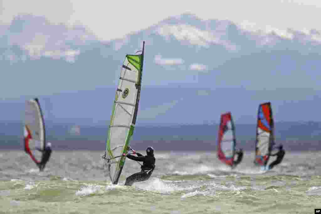 Surfers brave high winds to speed on the waves at lake Ammersee in front of the Alps near Herrsching, Germany.
