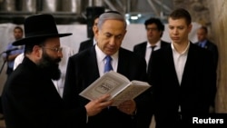 FILE - Israel's Prime Minister Benjamin Netanyahu, center, reads a prayer with Western Wall Rabbi Shmuel Rabinowitz, left, as his son Yair, right, stands next to him, at the Western Wall, in Jerusalem's Old City, March 18, 2015.