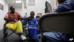 FILE - Ali Said, of Somalia, left, waits at a center for refugees with his two sons, July 6, 2017, in San Diego. Said, whose leg was blown off by a grenade, says he felt unbelievably lucky to be among the last refugees allowed into the United States before stricter rules kicked in as part of the Trump administration's travel ban.