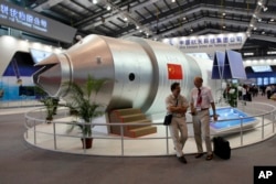 Visitors sit beside a model of Chinese-made Tiangong 1 space station at the 8th China International Aviation and Aerospace Exhibition, known as Airshow China 2010, in Zhuhai city, south China, Guangdong province, Nov. 16, 2010.