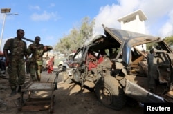 FILE - Somali policemen look at the wreckage of a car at the scene of an explosion following an attack in Somalia's capital Mogadishu, March 9, 2016.