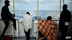 FILE - Migrants look at the coastline as they stand aboard a rescue ship, off the coast of Sicily, May 14, 2018. 