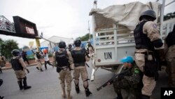 Foto Archivo - Un guardia de paz de Estados Unidos se esconde detrás de los policías nacionales mientras los manifestantes lanzan piedras durante una protesta contra el consejo electoral del país para celebrar el 25 aniversario de la primera elección democrática en 1990 en Puerto Príncipe, Haití.